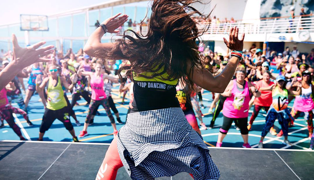 Woman leading a Zumba class with her hands in the air and a packed class of people doing the same