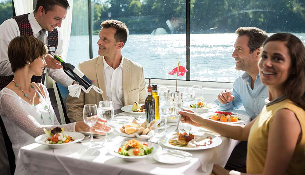 Two couples sit at a restaurant table while a server presents a bottle of wine