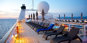 Top deck of a cruise ship featuring many loungers and lights at sunset