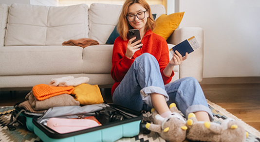 Woman on phone planning travel with passport and suitcase