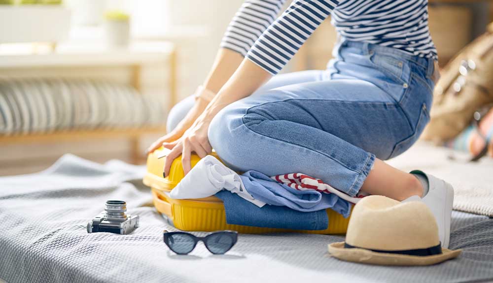 A woman sits on top of her suitcase to try and close it