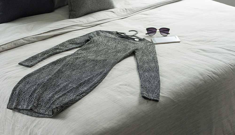 A dress and sunglasses are shown laid out on a bed