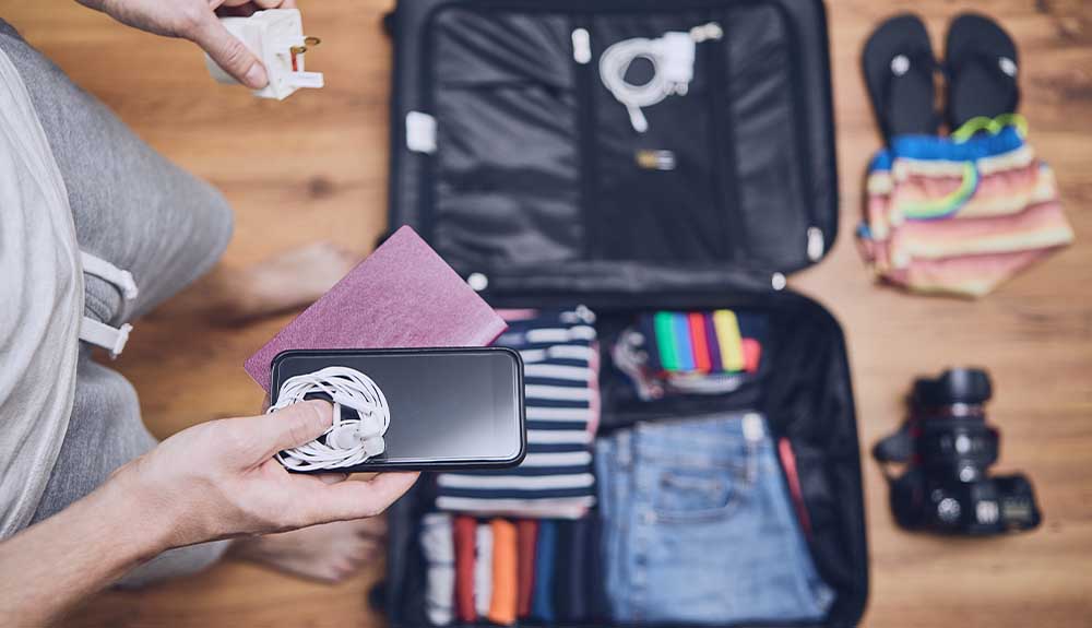 A man is shown packing gadgets into his suitcase