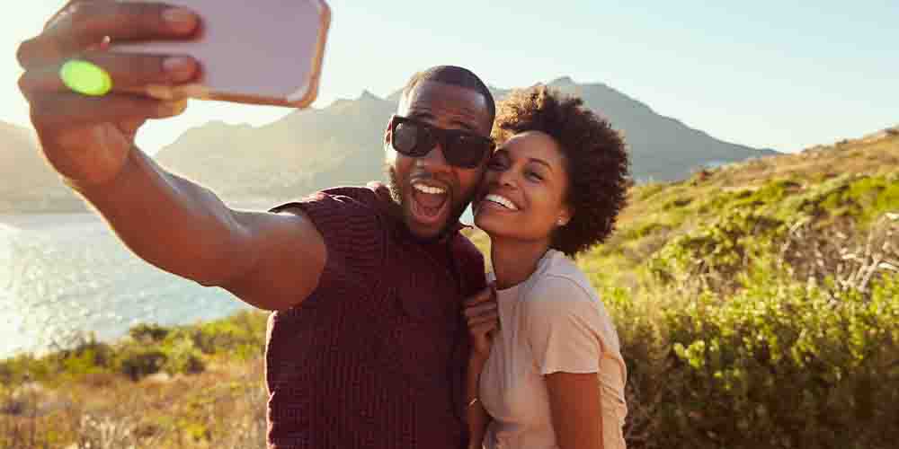 A couple pose for a selfie with water and mountains in the background