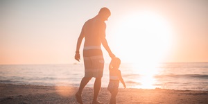 A father and young daughter walk along the beach at sunset