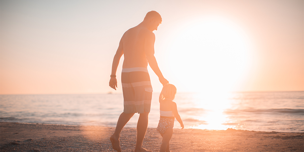A father and young daughter walk along the beach at sunset