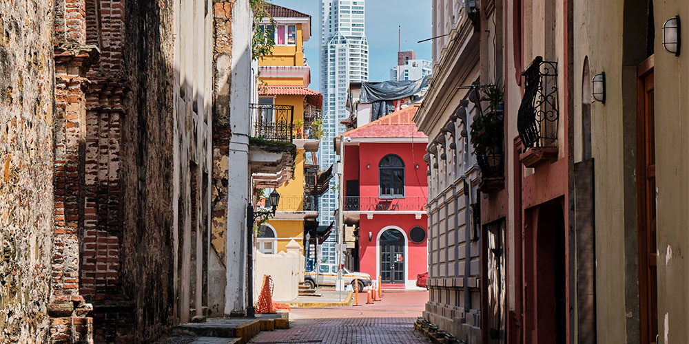 A view down an alley in Panama City, at the end of the alley are brightly coloured buildings.