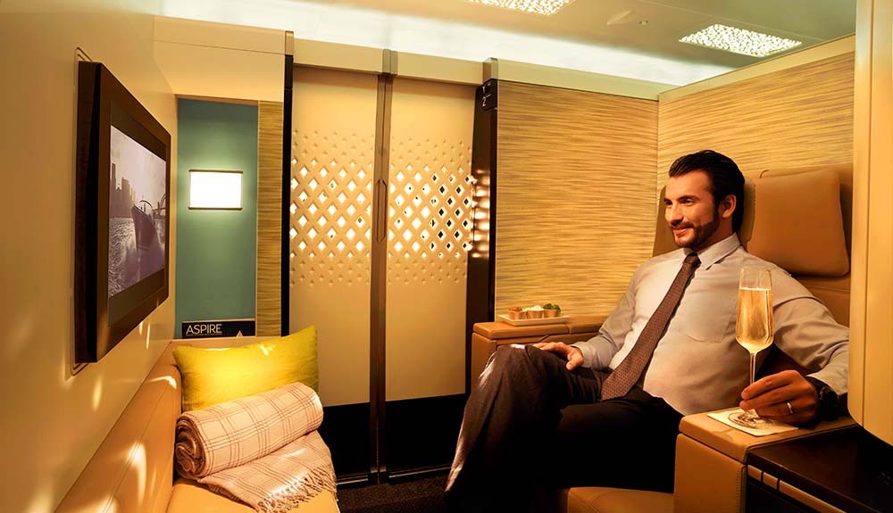 A man sits in a private apartment compartment watching a movie with a glass of champagne on Etihad Airlines