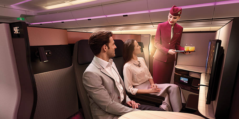 A man and women sit in large, luxurious seats as a flight attendant serves them a drink