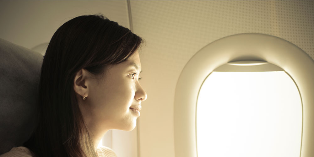 A woman looks out a bright airplane window
