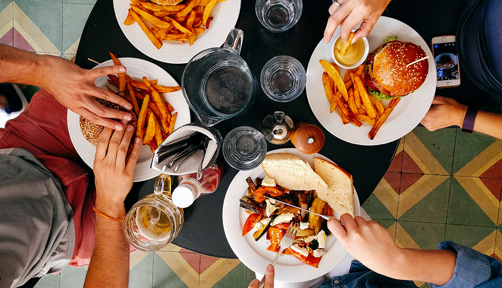 An overhead shot of four plates, three with burgers and fries, one with a salad
