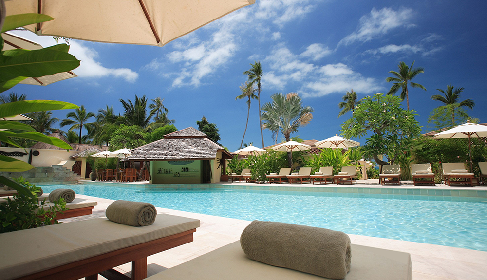 A resort pool, empty sun loungers under umbrellas lining the pool