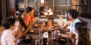 A large family claps in excitement while watching a chef prepare a dish at a Hibachi grill