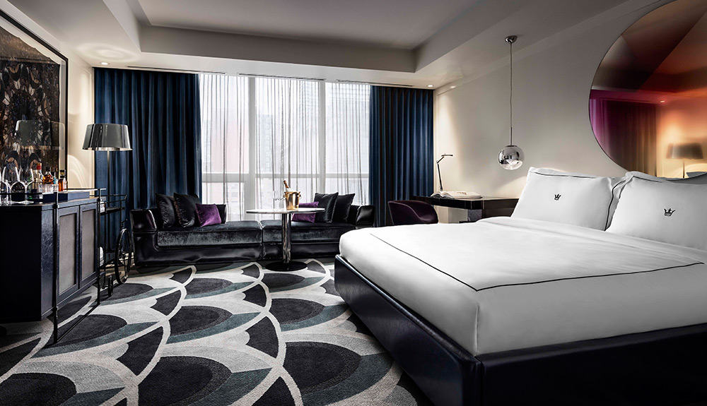 Large hotel suite with king sized bed, patterned carpet and navy blue drapes