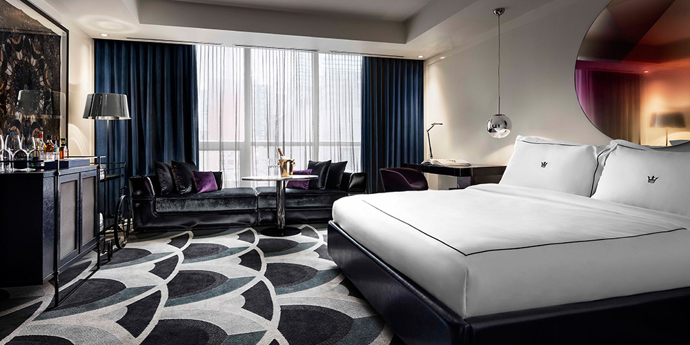 A trendy hotel suite with large bed, patterened carpet and navy blue drapes