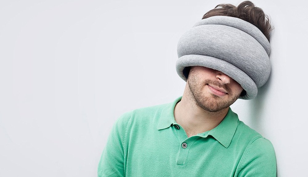 A man snoozes against the wall wearing the plush OstrichPillow Light over his eyes