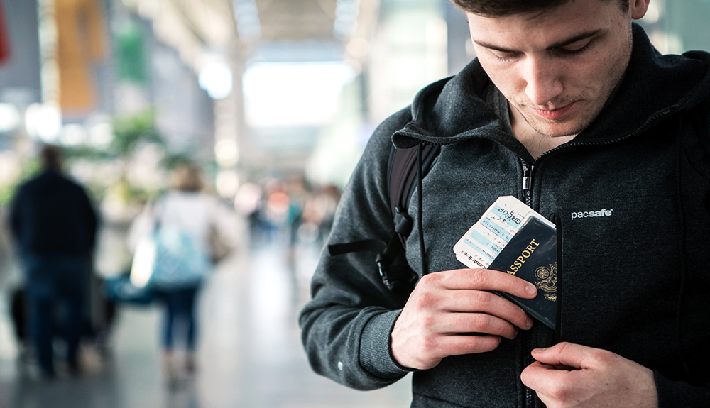 A man tucks his passport and boarding pass into the interior pocket of his PacSafe Transit jacket