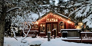 The exterior of a holiday cabin decorated with lights and wreaths with snow on the ground
