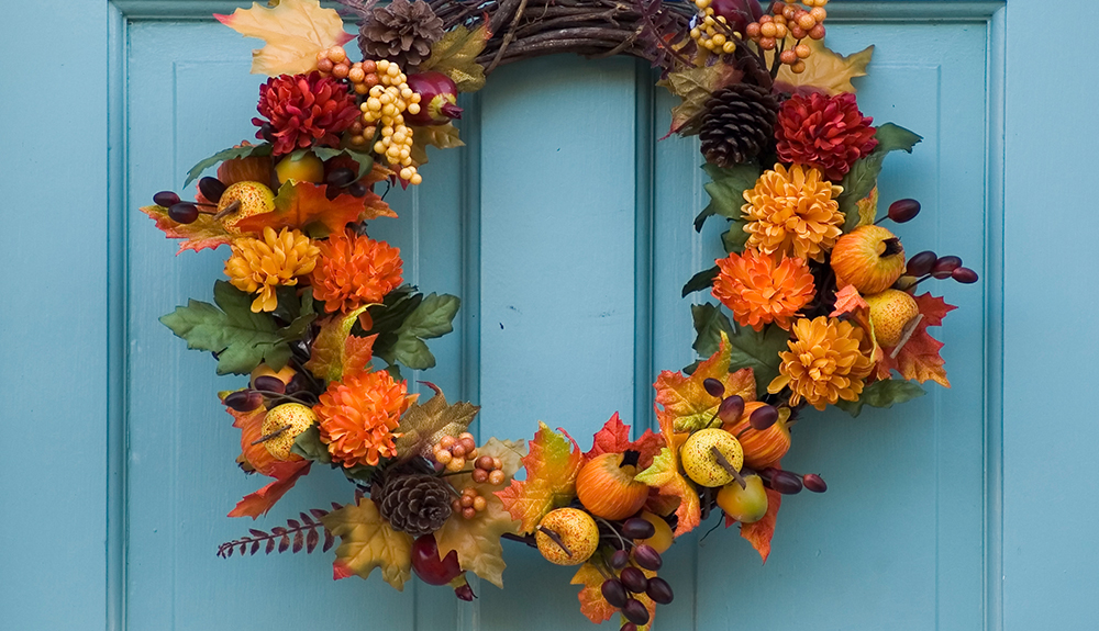 An orange fall harvest wreath hangs on a blue door