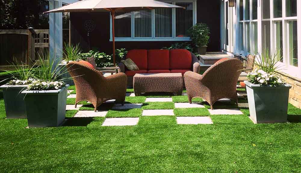 An outdoor lounge area over an artificial turf with an outdoor couch, wicker furniture and a large umbrella