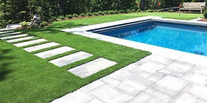A lawn with artificial turf and stone next to a blue pool