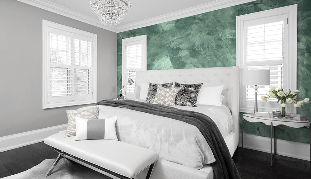 A bedroom with large bed with white headboard, a statement green textured wall behind the headboard