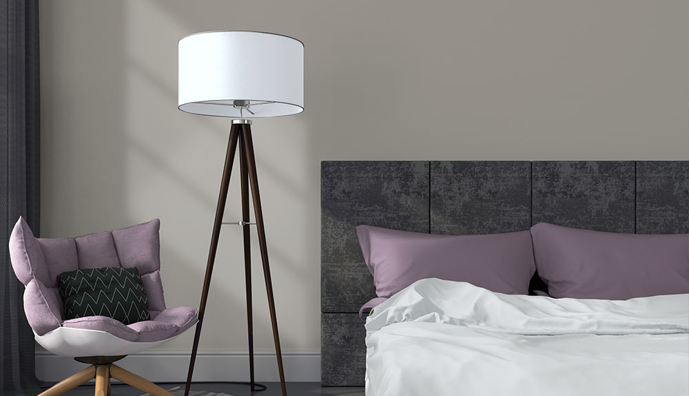 Neutral grey wall complements a dark grey headboard and purple pillows of a bedroom set, a matching purple chair sits in the corner near a black and white lamp