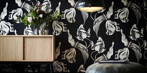 Dark floral wallpaper behind a light wood shelving unit with fresh flowers on top