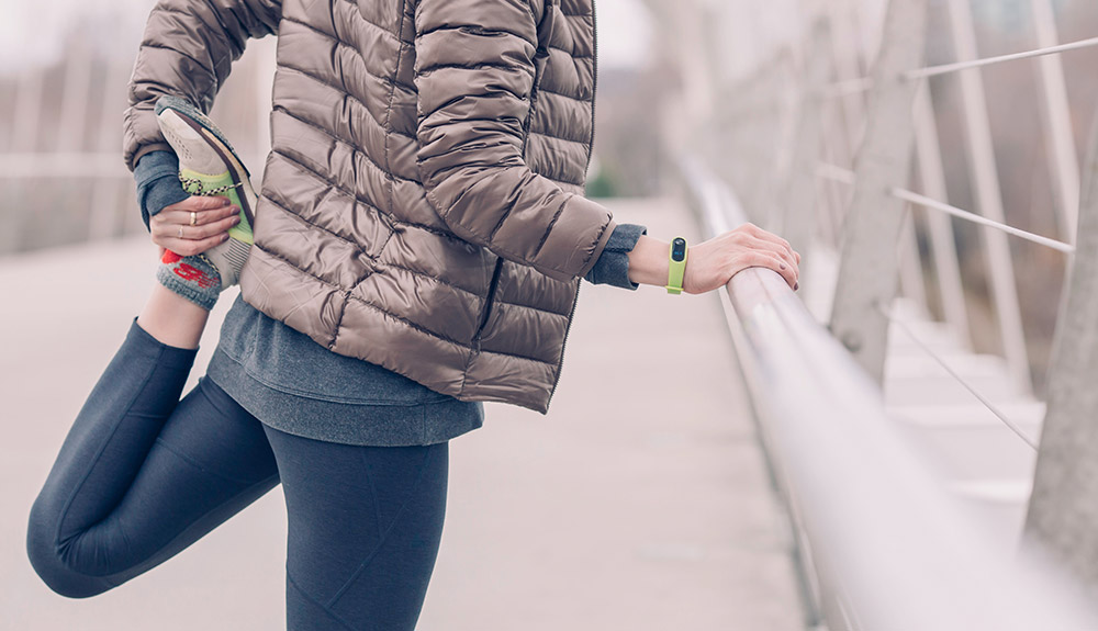 Woman stretching her leg outside in the winter on a bridge