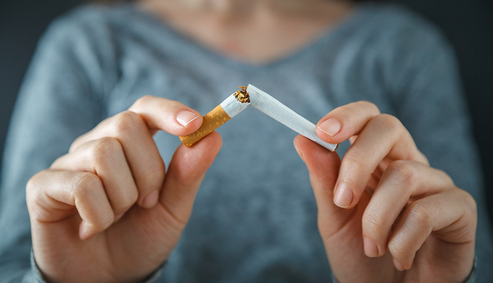 Woman snapping an orange filtered cigarette in half