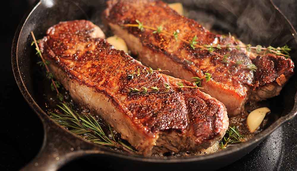 A pork chop with a sprig of rosemary cooks in a cast iron pan