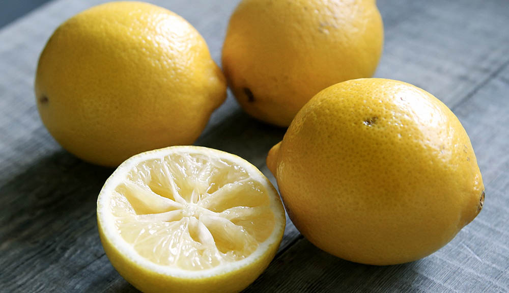 Three whole lemons on a counter, one half a lemon, already juiced
