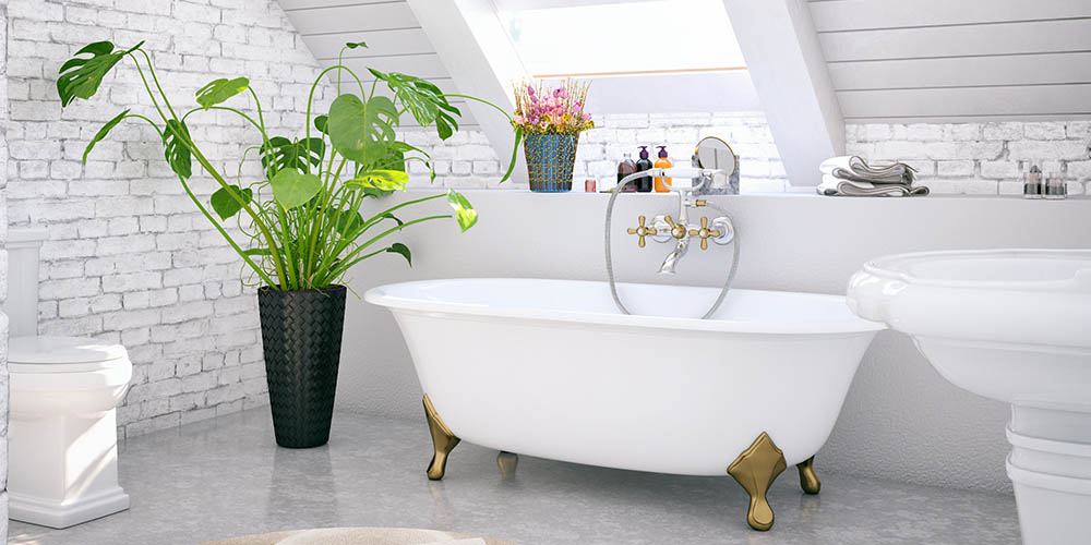 Clawfoot tub with gold feet in a bright washroom next to a plant in the daytime