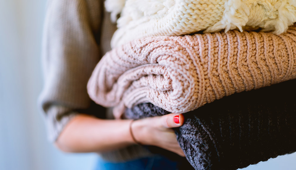 Woman carrying white, pink and black sweaters stacked in her hands