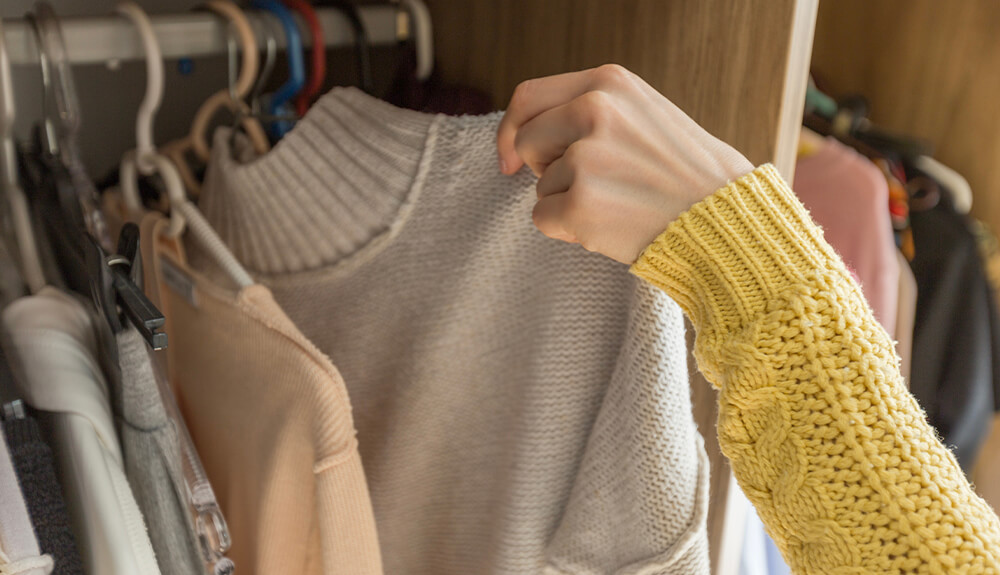 Person lifting sweater on hanger out of closet