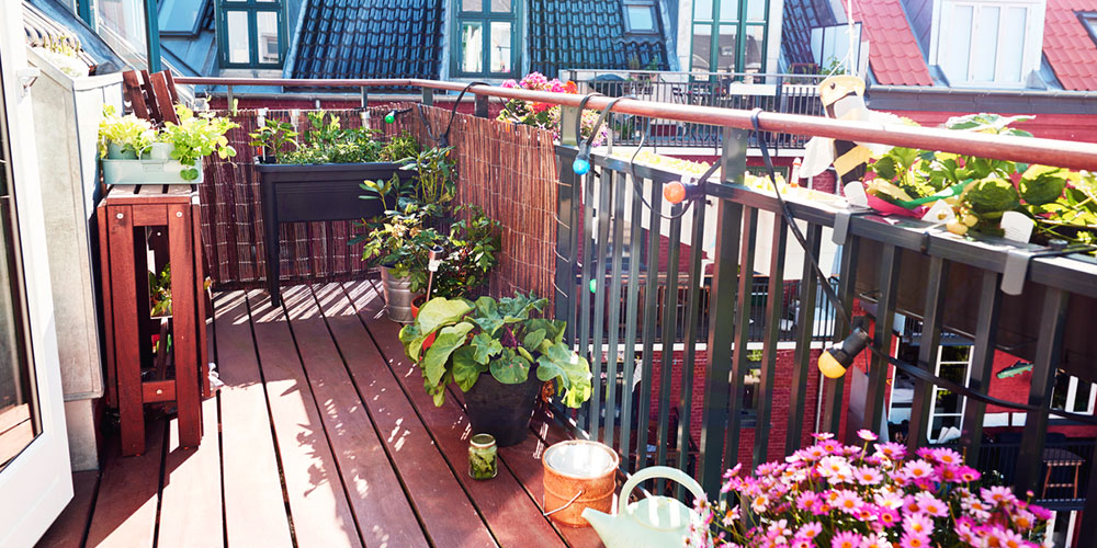 Pink flowers, round and rectangular potted plants fill a small wooden balcony