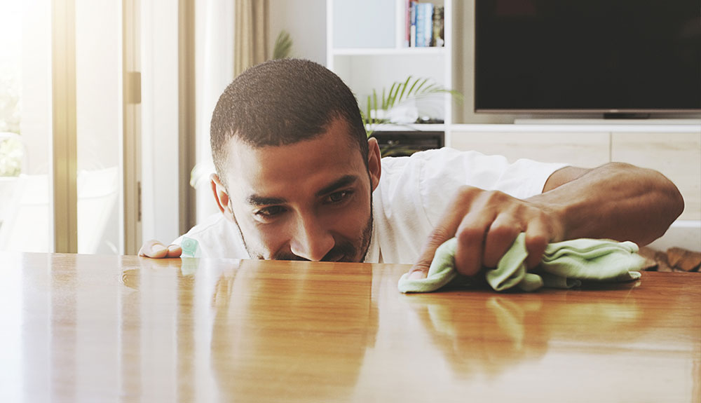 Man crouches next to a table as he cleans it