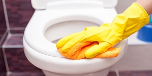 Gloved hand holding a cleaning towel against a toilet seat
