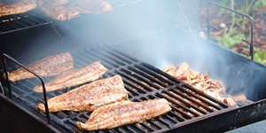 Four fish fillets on a hot grill as smoke fills the barbecue