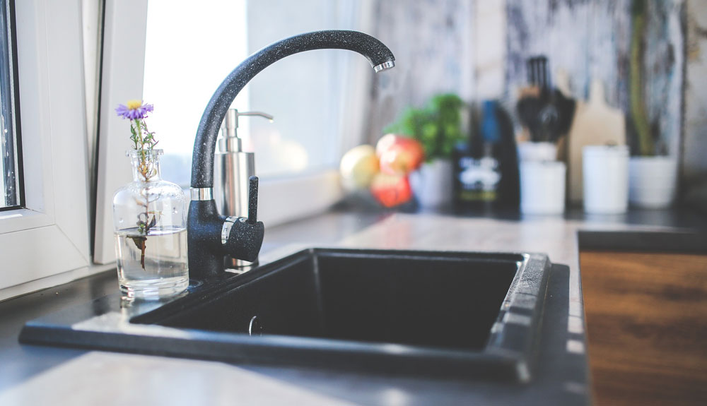 Side shot of the faucet of a kitchen sink by a window in the daylight
