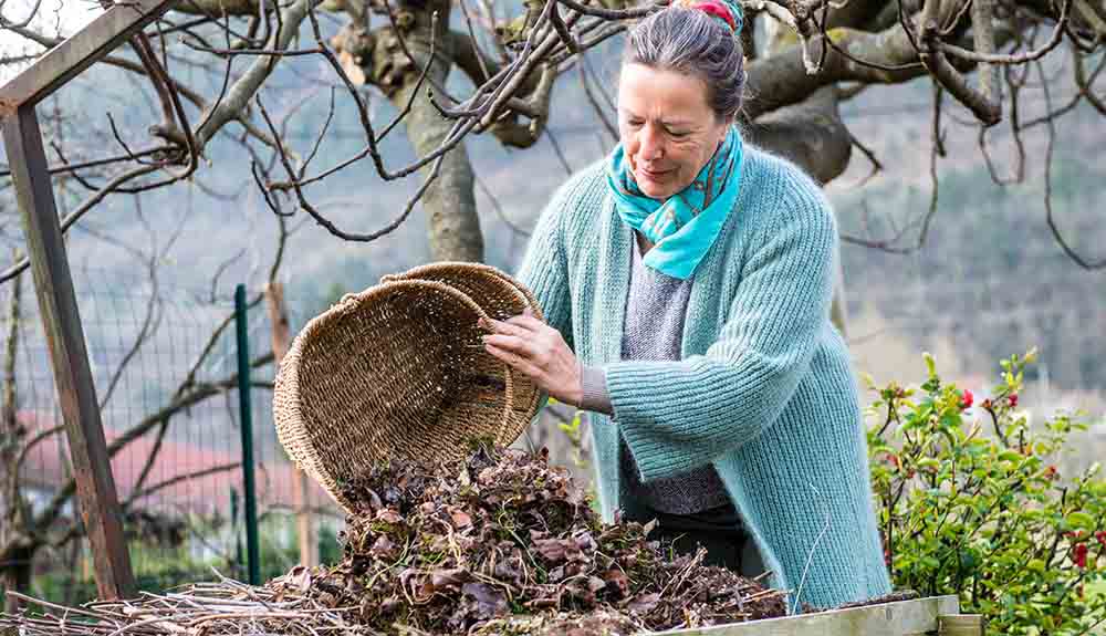 A woman empties a basket of leaves onto a table outdoors.