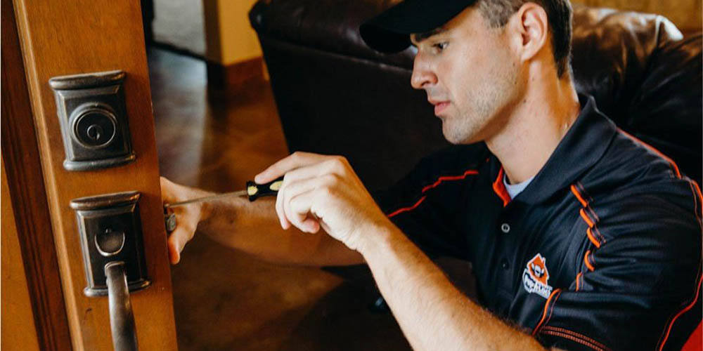 A locksmith adjusts a lock on a wooden door.