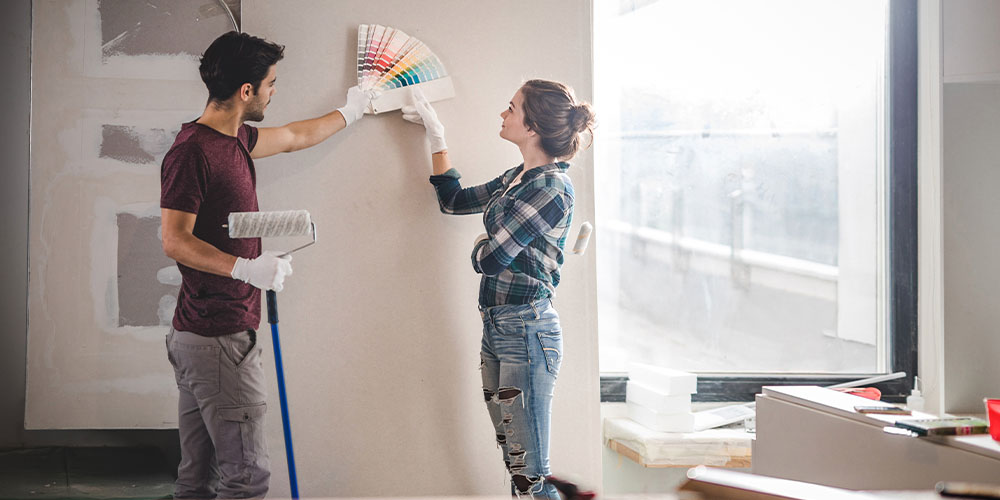 A couple look at paint chips against their beige wall.