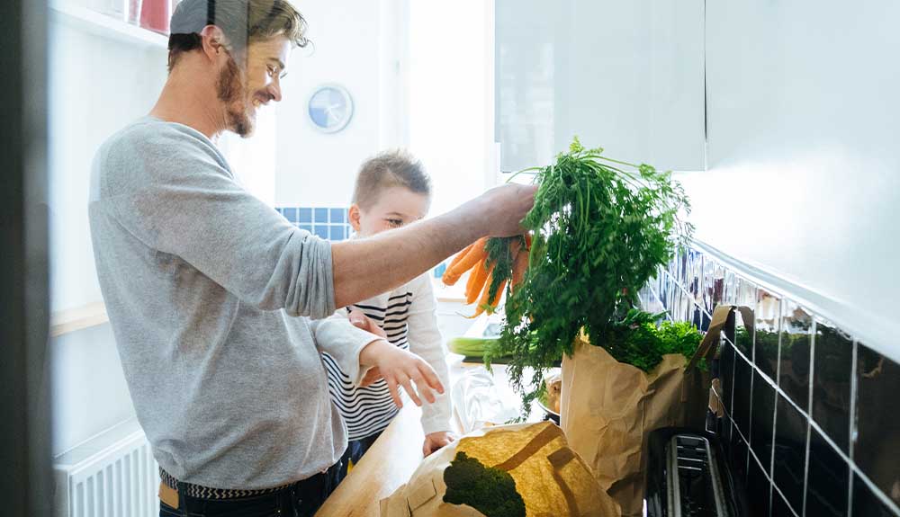 A father and son are shown unpacking groceries in their kitchen