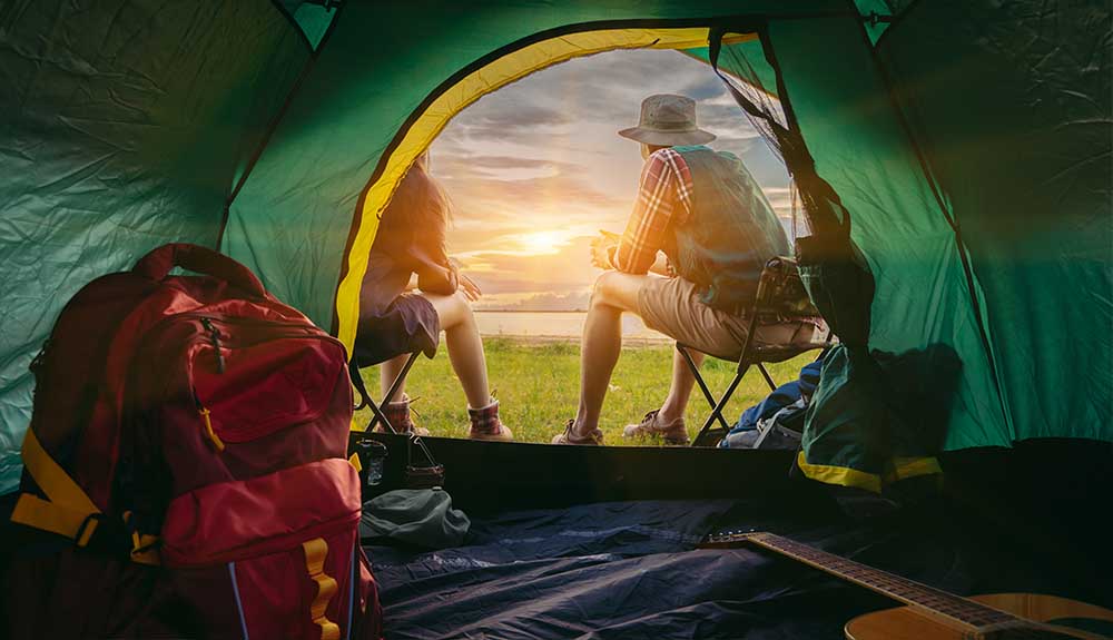 Two people are shown sitting outside their camping tent