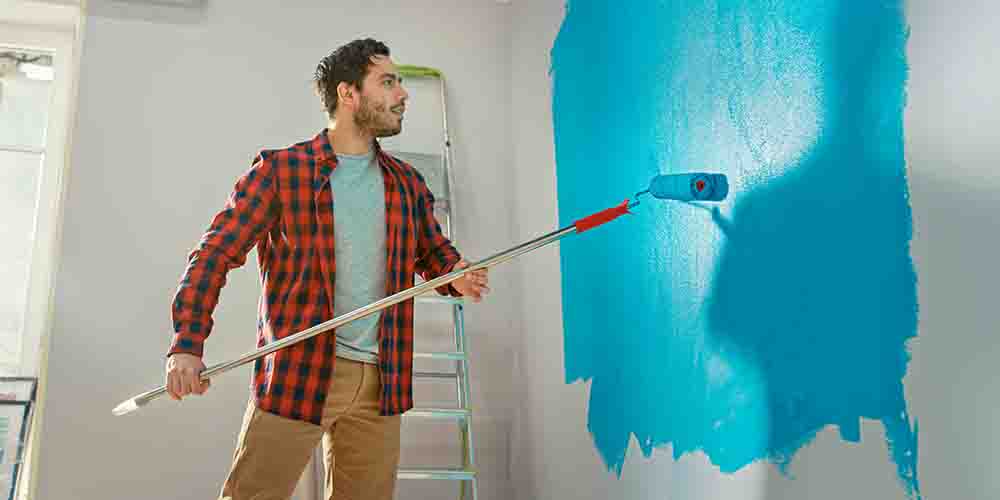 A man paints a white wall a teal blue colour