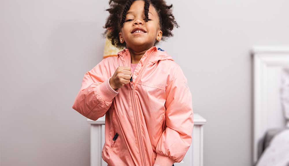 A child is shown zipping up a pink jacket