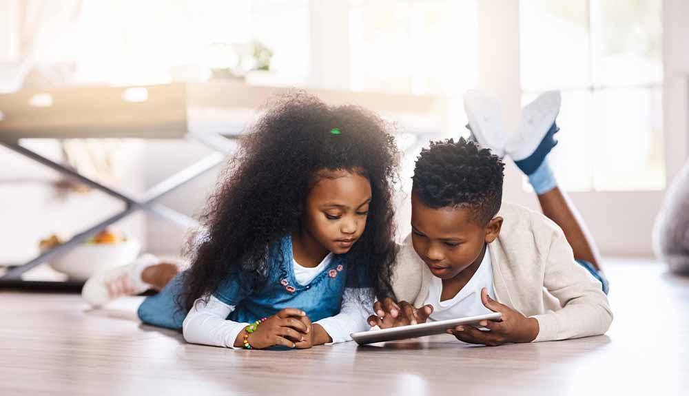 A young boy and girl look at a tablet together on the floor