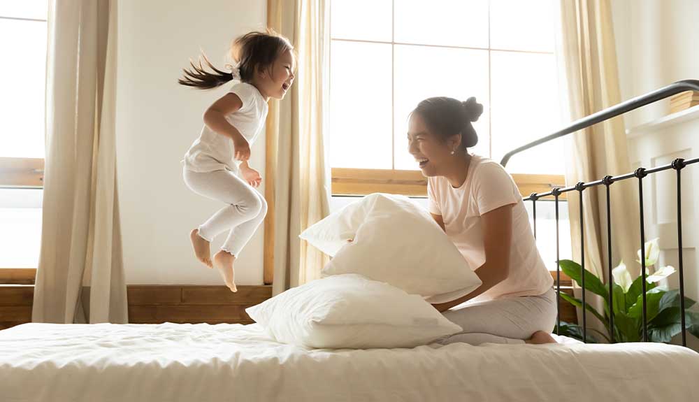 A child jumps on a bed while her mother looks on