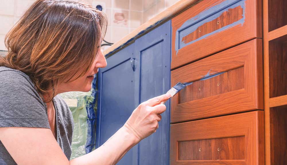A woman paints her kitchen cabinets blue
